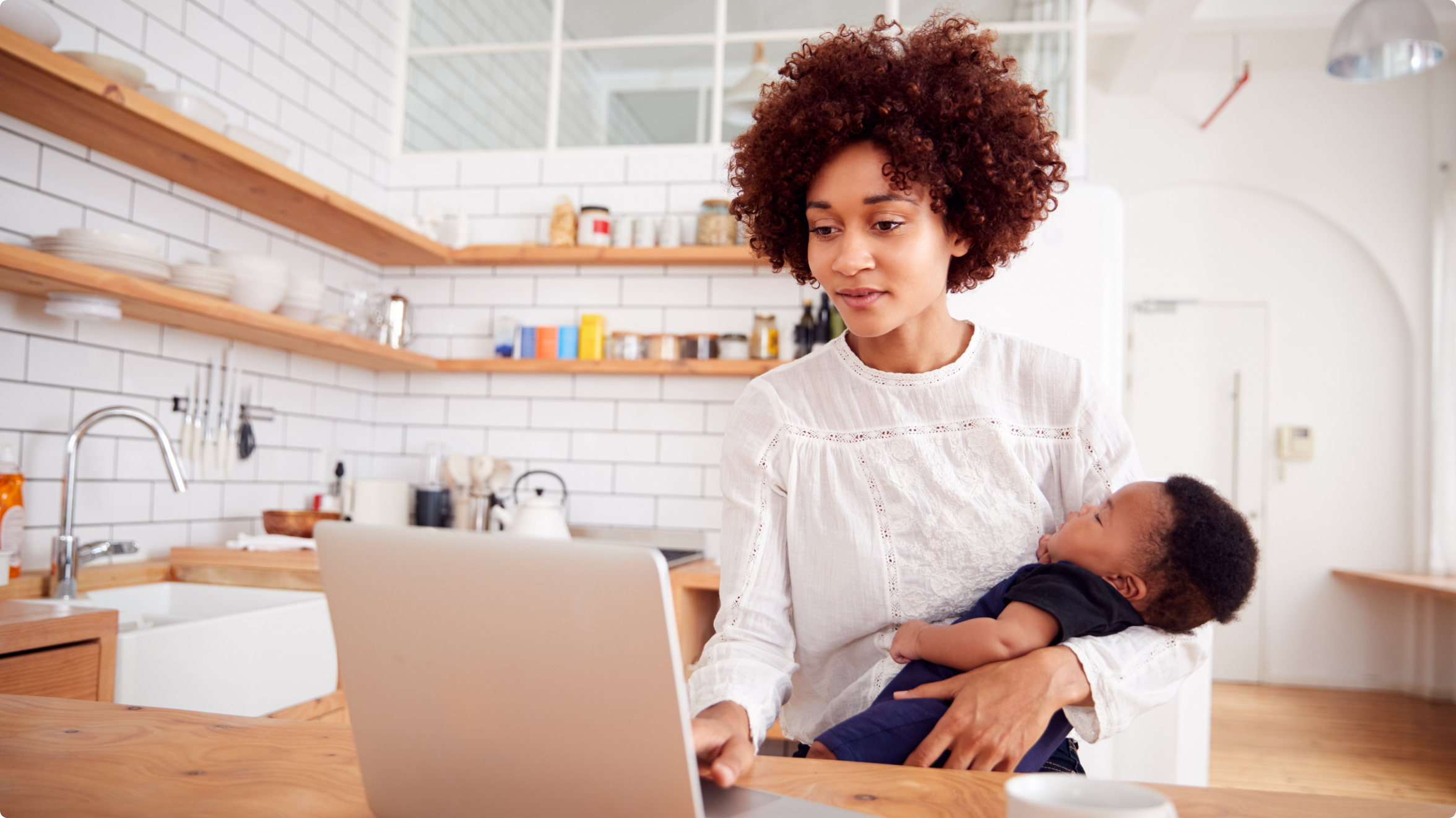 woman holding a baby while using a laptop