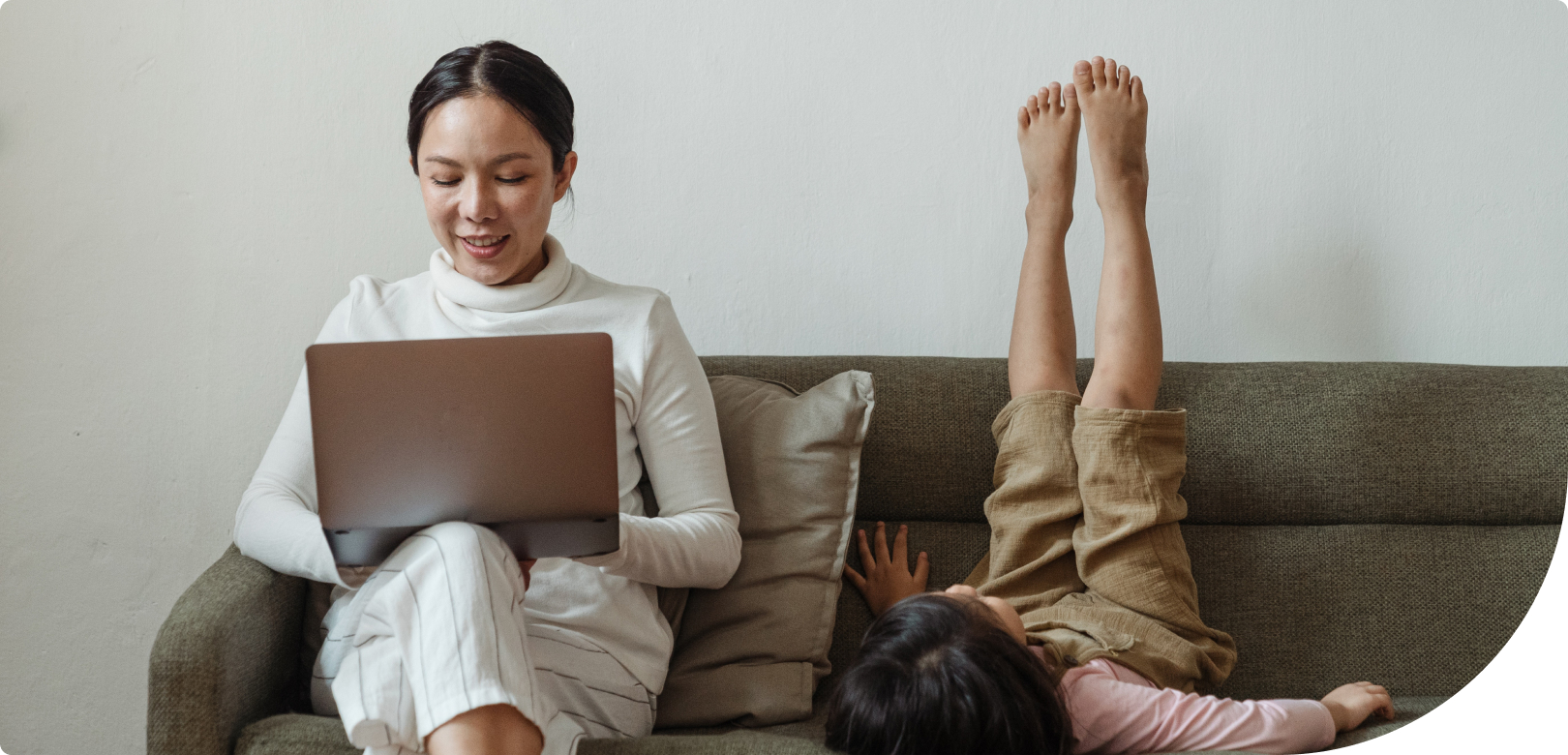 woman on couch looking at laptop next to a child laying upside down