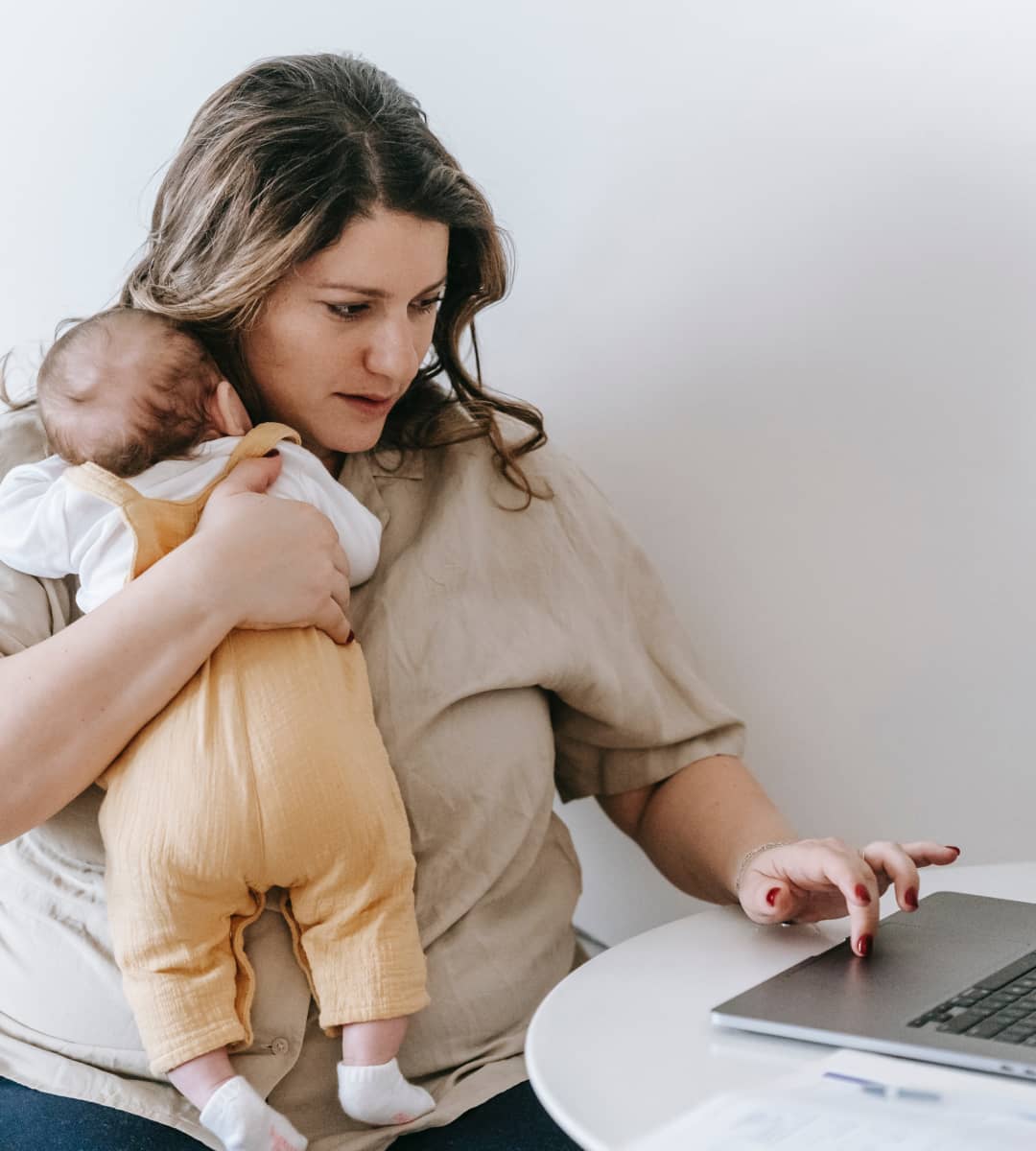Mother holding her baby while doing something in her laptop