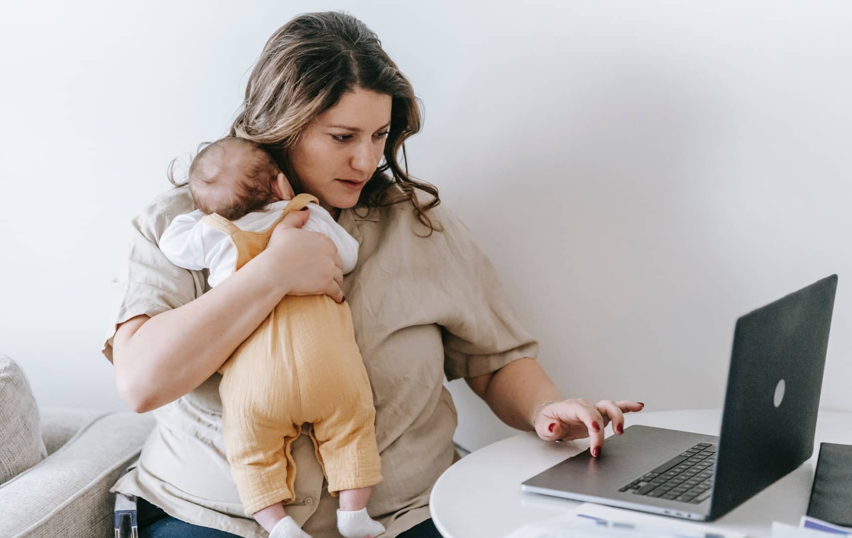 picture of a woman doing something in her laptop while holding her baby