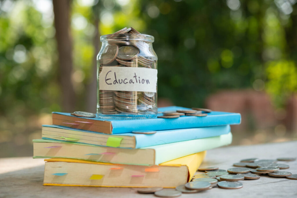 Jar of coins labeled ‘Education’ placed on top of stacked books representing tuition costs