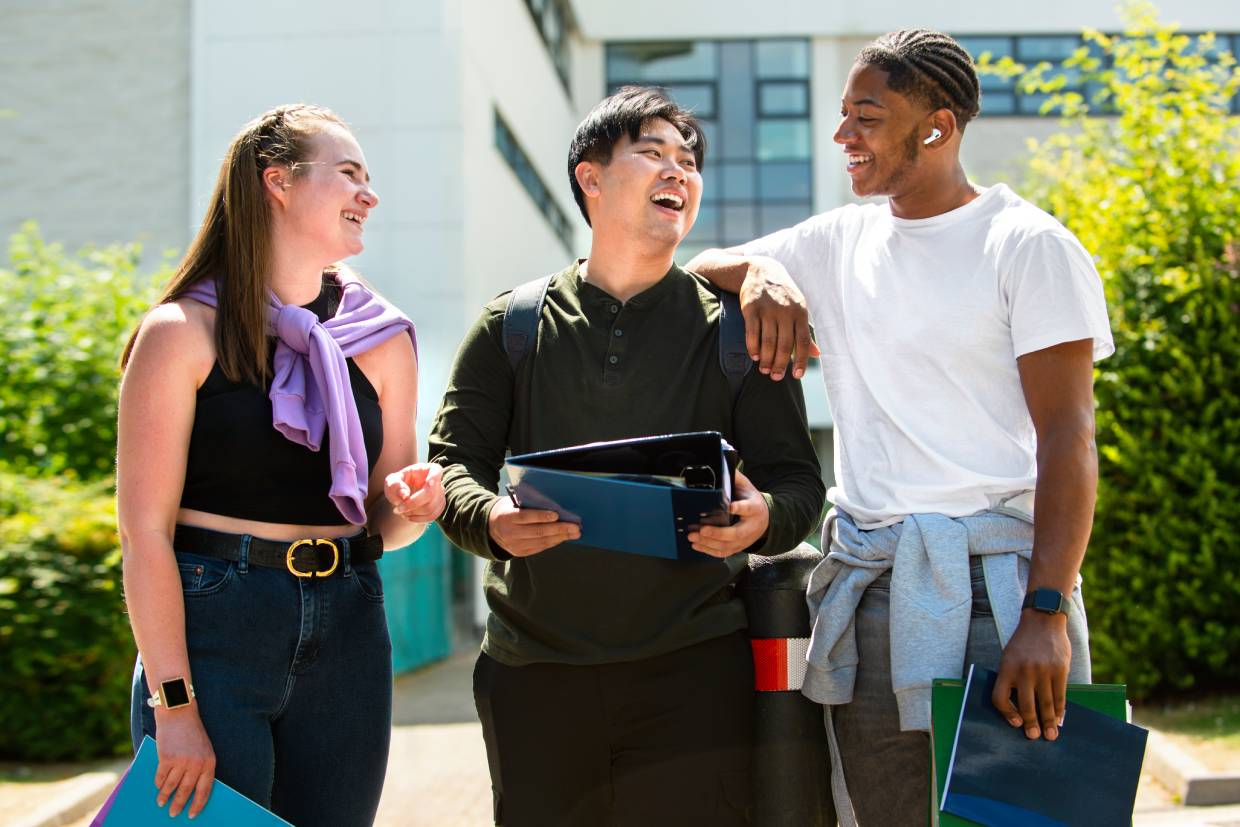 Three graduate students smiling and talking on campus, representing Amberton University’s flexible pay-as-you-go tuition model.